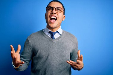 Kravat takan genç Brezilyalı işadamı, izole edilmiş mavi arka planda deli deli deli bağırıyor ve agresif bir ifadeyle bağırıyor ve kollarını kaldırıyor. Hayal kırıklığı konsepti.