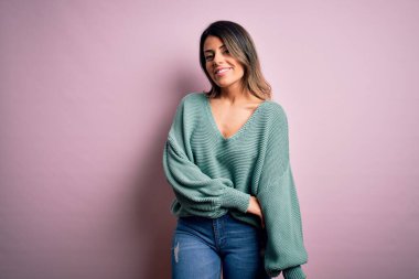 Moda kıyafetleri giyen genç ve güzel bir kadın. Manken, sokak tarzı giyiniyor. Pembe arka planda dikiliyor.