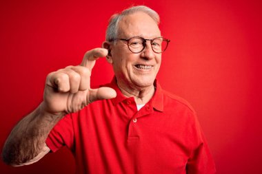 Gri saçlı, gözlüklü, kırmızı arka planda rahat tişörtlü, gülümseyen, kendine güvenen, el hareketi yapan, parmaklarıyla işaret yapan ve kameraya bakan son sınıf öğrencisi. Ölçü kavramı.