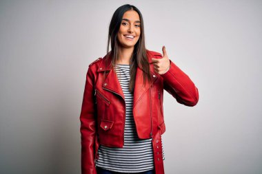 Genç, güzel, esmer, sıradan çizgili tişört ve kırmızı ceket giyen bir kadın. Elle mutlu bir jest yapıyor. Kameraya bakıp başarıyı gösteren ifade onaylanıyor.