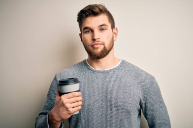 Sakallı, mavi gözlü, beyaz arka planda bir fincan kahve içen zeki yüzlü, kendine güvenen, ciddi düşünen genç sarışın bir adam.