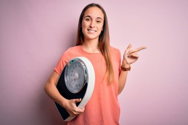 Ağırlık ölçme makinesini pembe arka planda kontrol eden genç ve güzel bir kadın.