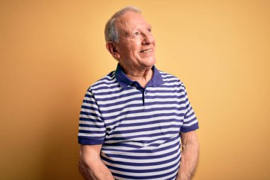 Gri saçlı, donanma çizgili tişört giyen, sarı arka planda duran, yüzünde gülümseme ve doğal bir ifadeyle yan yana bakan son sınıf öğrencisi. Kendinden emin gülen.