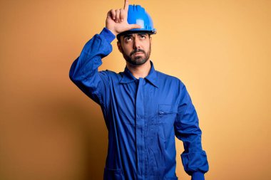 Sakallı, mavi üniformalı ve sarı arka planda kasklı tamirci. Alnında parmakları olan insanlarla alay ediyor. Ezik hareketler yapıyor, alay ediyor ve hakaret ediyor..