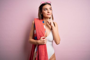Kumsal havlusu ve güneş gözlüğü takmış, tatilde olan genç, güzel esmer kadın soru soran ciddi bir yüz, çok karışık bir fikir.
