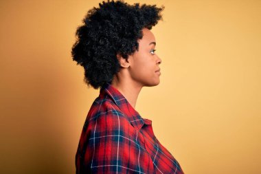 Young beautiful African American afro woman with curly hair wearing casual shirt looking to side, relax profile pose with natural face with confident smile.