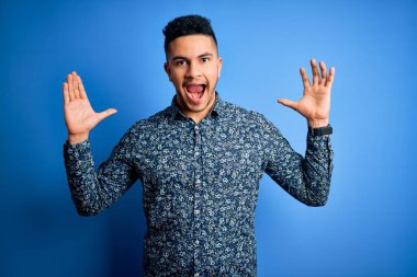 Genç ve yakışıklı bir adam, yalnız mavi arka planda dikilip kollarını kaldırıp heyecanla haykırarak çılgınca ve hayret verici bir başarıyı kutluyor. Kazanan konsept