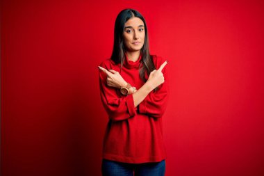 Genç, güzel esmer kadın izole edilmiş kırmızı arka plan üzerine gündelik süveter giyiyor. Her iki tarafı da parmaklarıyla işaret ediyor. Farklı yönler farklı.