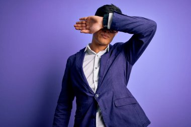 Ceket ve gözlük takan genç yakışıklı iş adamı mor arka planda gözleri kolla kaplıyor, ciddi ve üzgün görünüyor. Görme, saklama ve reddetme konsepti