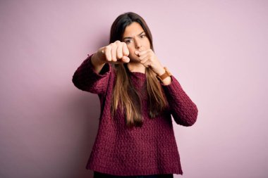 Genç, güzel bir kız pembe arka plan üzerine günlük süveter giyiyor. Yumruğunu yumrukluyor, saldırıyor, saldırıyor, tehdit ediyor ve şiddet uyguluyor.