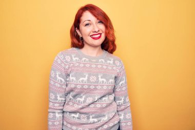 Güzel kızıl saçlı kadın, sarı arka planda ren geyiğiyle Noel süveteri giyiyor ve yüzünde mutlu ve havalı bir gülümseme var. Şanslı kişi..