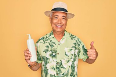 Orta yaşlı, kır saçlı, yaz şapkası takan, güneş kremi kullanan, mutlu, gülümseyen, işaret veren, parmaklarıyla başparmağını kaldıran yaşlı bir adam.