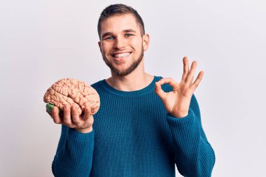 Beyni tutan yakışıklı genç adam parmaklarıyla işaret yapıyor, gülümseyerek mükemmel bir sembol oluşturuyor. 