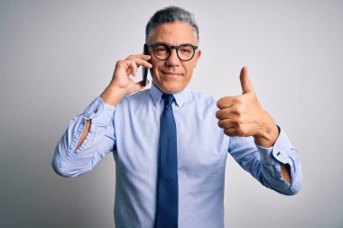 Orta yaşlı, yakışıklı, gri saçlı iş adamı akıllı telefondan konuşuyor. Kocaman gülümsüyor, gülümsüyor. İşaret veriyor.