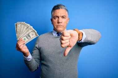 Orta yaşlı, yakışıklı, gri saçlı, elinde bir tomar dolar tutan, kızgın yüzlü, olumsuz işaretli, baş parmakları aşağıda, reddedilme konsepti olan bir adam.