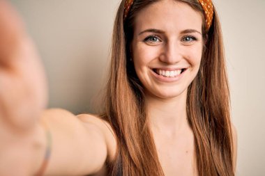 Diadem takan genç, güzel, kızıl saçlı bir kadın kameranın önünde mutlu bir yüz ifadesiyle özçekim yapıyor. Kendine güvenen bir gülümsemeyle dişlerini gösteriyor.