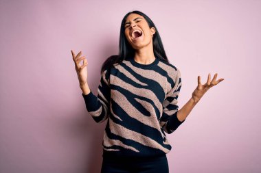 Pembe arka planda hayvan desenli süveter giyen genç ve güzel bir İspanyol kadın. Deli gibi bağırıyor ve agresif bir ifade ve kollarla bağırıyor. Hayal kırıklığı konsepti.