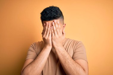 İzole edilmiş sarı arka plan üzerinde duran sıradan tişört giyen genç yakışıklı bir adam. Ağlarken suratını ellerle kapatan üzgün bir ifade. Depresyon kavramı.
