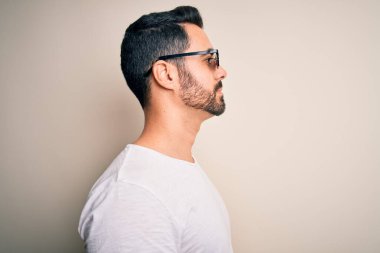 Sakallı, komik, cani hayat gözlüğü takan beyaz arka plan üzerine bakan yakışıklı genç bir adam, rahat profil pozu, kendine güvenen bir gülümsemeyle doğal bir poz..