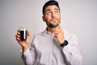Genç yakışıklı bir adam, beyaz izole edilmiş arka planda bir fincan sıcak kahve içiyor ciddi bir yüz düşünüyor, kafası karışmış bir fikir.