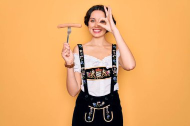 Mavi gözlü genç Alman kadın Ekim Festivali elbisesi giyiyor elinde çatal, mutlu yüzlü sosisli ve gülümseyen.