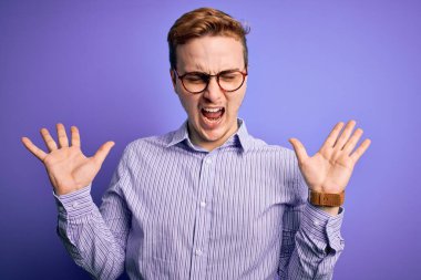 Mor arka plan üzerine gündelik gömlek ve gözlük takan genç, yakışıklı kızıl adam kollarını kaldırmış ve gözleri kapalı heyecanla haykırarak başarıyı kutluyor. Kazanan konsept