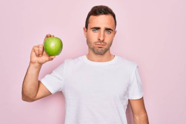 Genç, mavi gözlü, sağlıklı yeşil elma yiyen, soyutlanmış pembe arka planda kendine güvenen, akıllı yüzlü, ciddi düşünen yakışıklı bir adam.