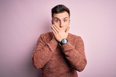 Pembe izole arka plan üzerine sıradan bir kazak giyen yakışıklı beyaz bir adam ağzını yanlışlıkla ellerle kapatarak şok etti. Gizli konsept.