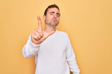 Mavi gözlü genç adam sarı arka planda dikilen sıradan bir süveter giyiyor. Parmakla işaret ediyor ve kızgın bir ifade sergiliyor.