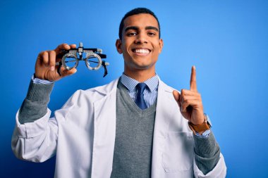 Yakışıklı afro-amerikan optik adam elinde optometri gözlüklerini mavi arka planda tutarken bir fikre ya da soru işaretine şaşırdı.