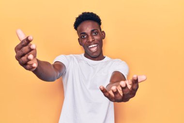 Gündelik giysiler giymiş genç Afro-Amerikan bir adam kameraya sarılıp gülümseyerek bakıyor. Mutluluğu kucaklayan neşeli bir ifade.. 