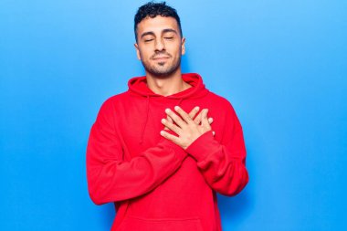 Gündelik kıyafetler giyen genç İspanyol adam elleri göğsünde gülümsüyor, gözleri kapalı ve yüzünde minnet ifadesi var. sağlık kavramı. 