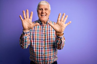 Kıdemli yakışıklı, beyaz gömlekli, yalıtılmış, mor arka planda, kendinden emin ve mutlu bir şekilde gülümserken on numarayı işaret eden adam..