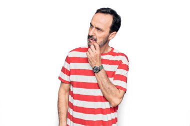 Orta yaşlı, çizgili tişört giyen yakışıklı bir adam izole edilmiş beyaz arka planda dikilirken parmak çenesinde şüpheye yoğunlaşır ve yukarı bakar.