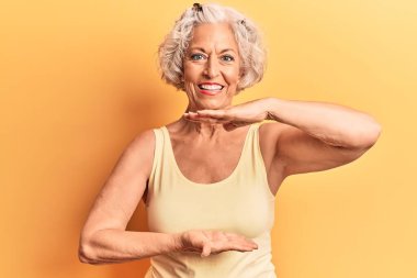 Yaşlı, gri saçlı, sıradan kıyafetler giyen, elleri büyük ve büyük beden işareti gösteren, ölçü sembolü olan bir kadın. Kameraya bakıp gülümsüyor. ölçüm kavramı. 