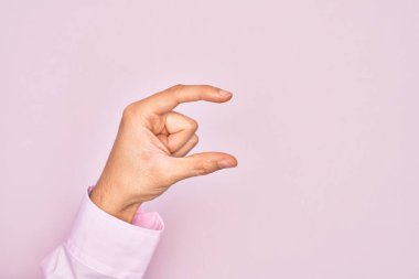 İzole edilmiş pembe arka plan üzerinde parmaklarını gösteren beyaz bir adamın eli. Görünmez bir şeyi alıp, parmaklarıyla uzayı gösteren bir nesneyi tutuyor.