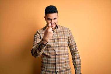 Sarı arka planda dikilen rahat tişörtlü genç yakışıklı seni buraya davet ediyor mutlu ve güler yüzlü bir şekilde.