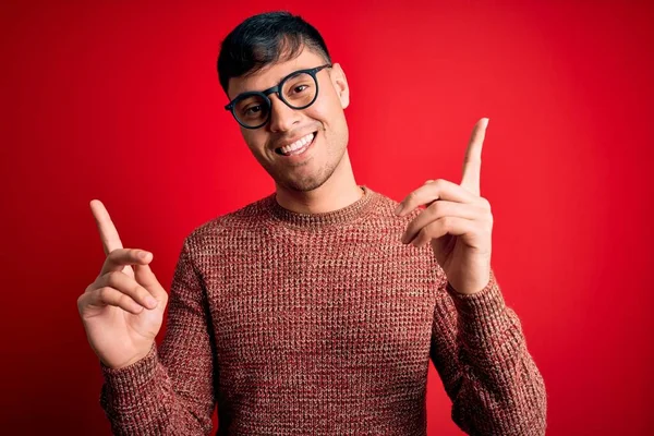 Mladý Pohledný Hispánec Šprtských Brýlích Červeném Pozadí Sebevědomě Usmívá Ukazuje — Stock fotografie