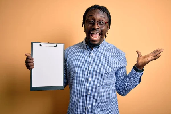 クリップボードのチェックリストを保持眼鏡を身に着けている若いアフリカ系アメリカ人の検査官の男は非常に幸せと興奮 大きな笑顔で叫んで勝利を祝う勝者式と手を上げ — ストック写真