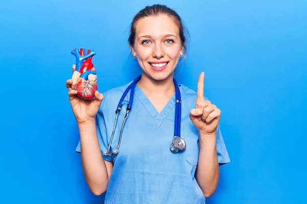 Doktor Üniforması Giyen Genç Sarışın Bir Kadın Elinde Kalp Gülümseyen — Stok fotoğraf