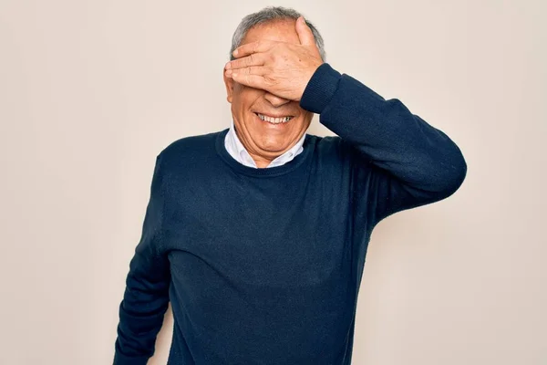 Senior handsome grey-haired man wearing sweater and glasses over isolated white background smiling and laughing with hand on face covering eyes for surprise. Blind concept.