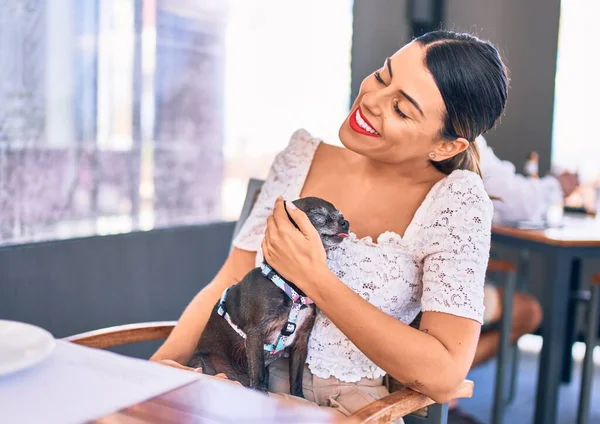若い美しいブルネットの女性は幸せと自信を笑顔 レストランでChihuahua犬を保持顔に笑顔でお座り — ストック写真