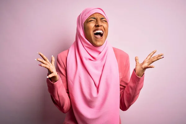 孤立したピンクの背景にイスラム教徒のヒジャーブを身に着けている若いアフリカ系アメリカ人のアフロ女性は 腕を上げて興奮して叫んで目を閉じて成功のために狂気と狂気を祝います 勝者のコンセプト — ストック写真
