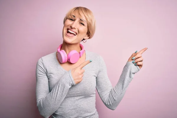 Młoda Blondynka Krótkimi Włosami Nosząca Słuchawki Szyi Różowym Tle Uśmiechnięta — Zdjęcie stockowe