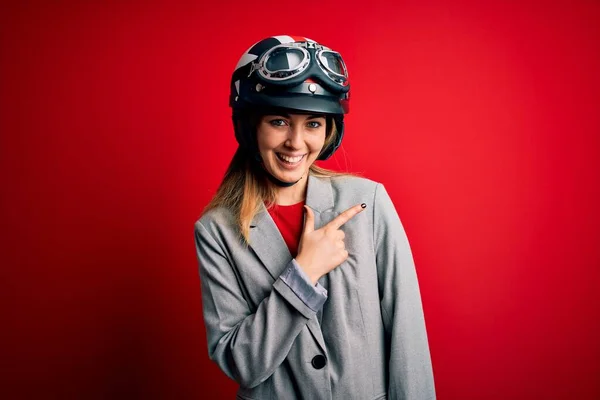 若いです美しいですブロンドオートバイのヘルメットを身に着けている女性上の赤い背景明るいです笑顔で顔を指して手と指で側まで幸せと自然な表現で顔 — ストック写真