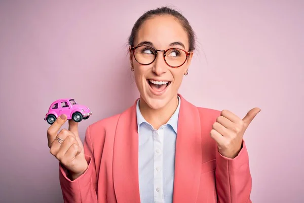 Νεαρή Όμορφη Επιχειρηματίας Φορώντας Γυαλιά Κρατώντας Ροζ Αυτοκίνητο Παιχνίδι Πάνω — Φωτογραφία Αρχείου