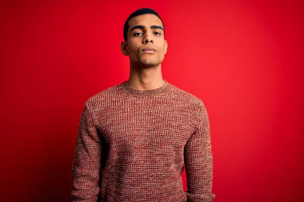 年轻英俊的非洲裔美国男人穿着宽松的毛衣站在红色的背景上 脸上带着严肃的表情 简单而自然地看着相机 — 图库照片