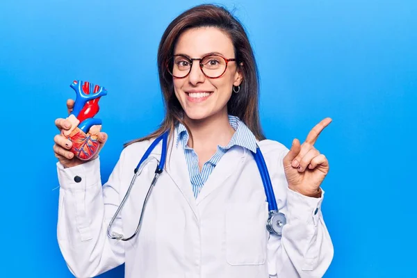 Mujer Hermosa Joven Que Lleva Doctor Stethoscope Sosteniendo Corazón Sonriendo —  Fotos de Stock