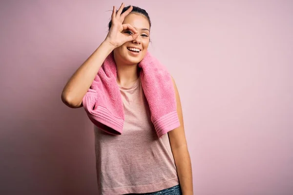 年轻美丽的黑发女运动员 身穿运动服 披着粉色背景的毛巾 手拿着手拿着手 微笑着 用手指看着她 面带微笑地看着她 — 图库照片