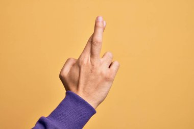 Kafkas genci parmaklarını izole edilmiş sarı arka plan üzerinde gösteriyor. Parmaklarını çapraz yapıyor, batıl inançlar ve şanslı bir jest, şanslı ve umut dolu bir ifade.